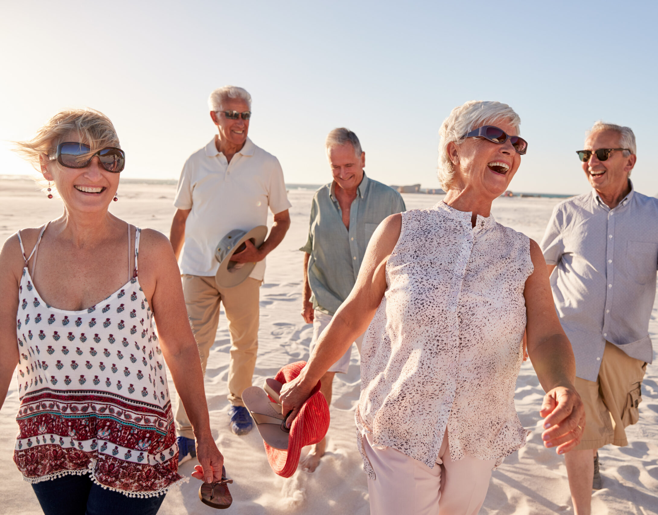Group Of Senior Friends Walking Along Sandy Beach On Summer Group Vacation